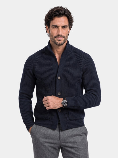 Man wearing a navy shawl-collar button knit jacket over gray trousers
