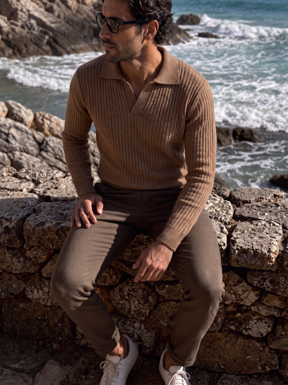 Man in the brown ribbed V-neck polo sweater seated outdoors
